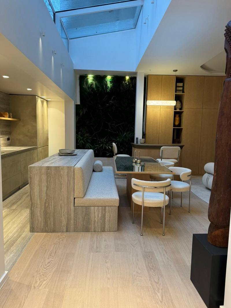Cuisine aux façades effet pierre, îlot en travertin prolongé d'une banquette tissu, table et chaises bouclette, mur végétal sous verrière