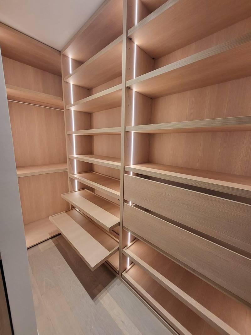 Dressing en bois clair : étagères, tiroirs, tablettes à chaussures sorties et penderie, montants éclairés par bandes LED verticales