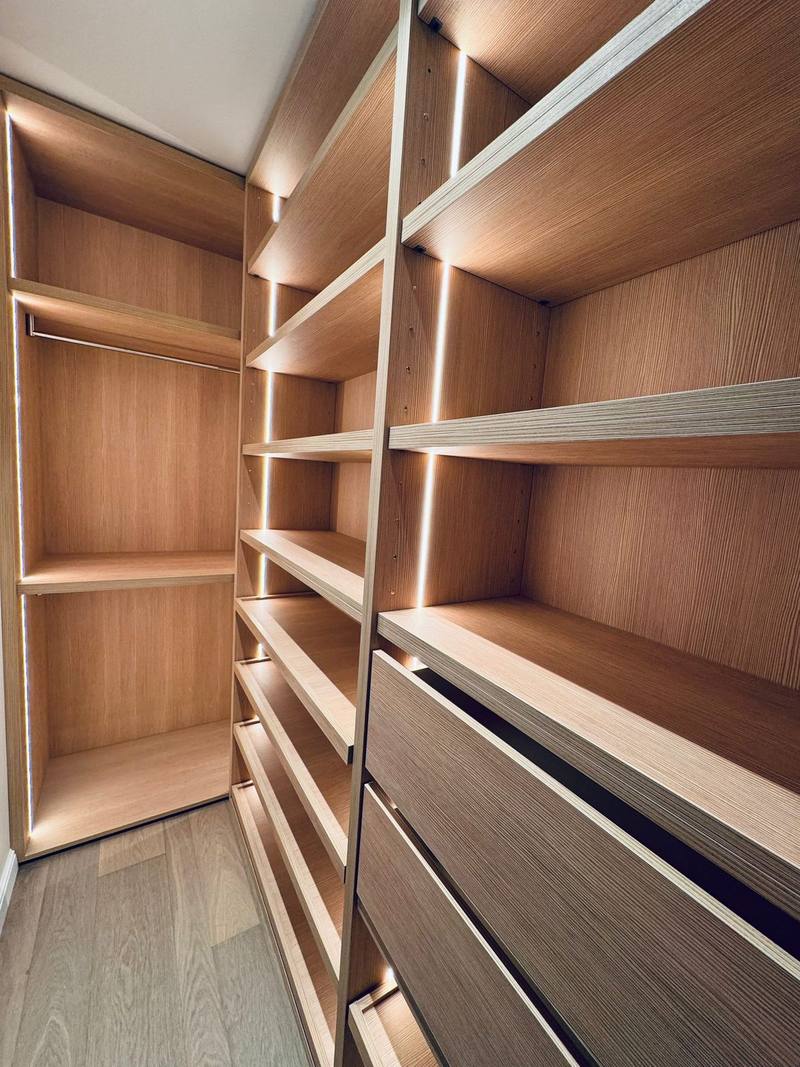 Dressing en bois clair avec étagères, penderie, tiroirs et tablettes à chaussures inclinées, éclairé par des rubans LED verticaux
