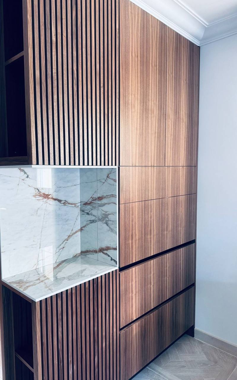 Meuble d'agencement toute hauteur en noyer, tasseaux verticaux, niche habillée de marbre veiné blanc et rouille, façades sans poignée