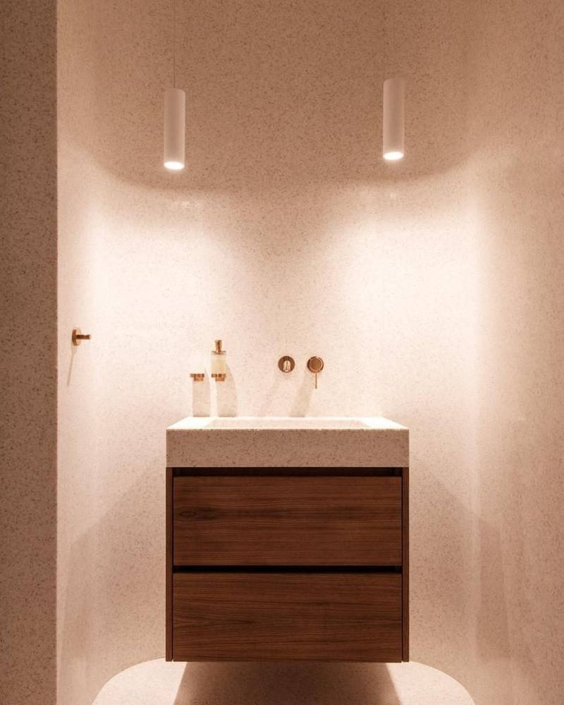 Meuble vasque suspendu en noyer à deux tiroirs, plan vasque type terrazzo clair, robinetterie murale cuivrée, deux suspensions blanches