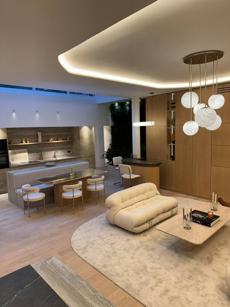 Pièce de vie ouverte : cuisine aux façades effet pierre, îlot avec banquette et table, mur de placards bois à niches éclairées, plafond à gorge lumineuse