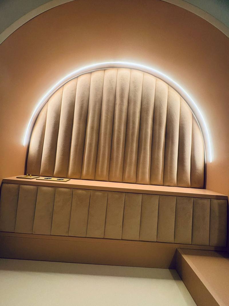 Niche en arche avec tête de lit capitonnée à côtes verticales en velours beige, liseré LED en arc et tablette de chevet intégrée avec interrupteurs et prises en laiton