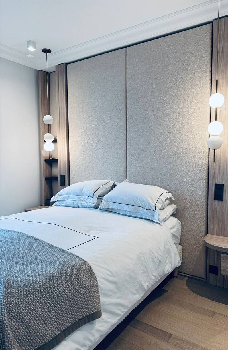 Chambre avec tête de lit en panneaux de tissu bouclette, montants bois clair, étagères sombres, chevets suspendus et suspensions en globes